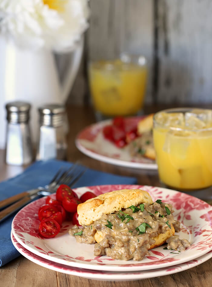 Tabletop Setting of Biscuits with Sausage and Maple Flavor White Gravy with Cherry Tomatoes and Glasses of Orange Juice