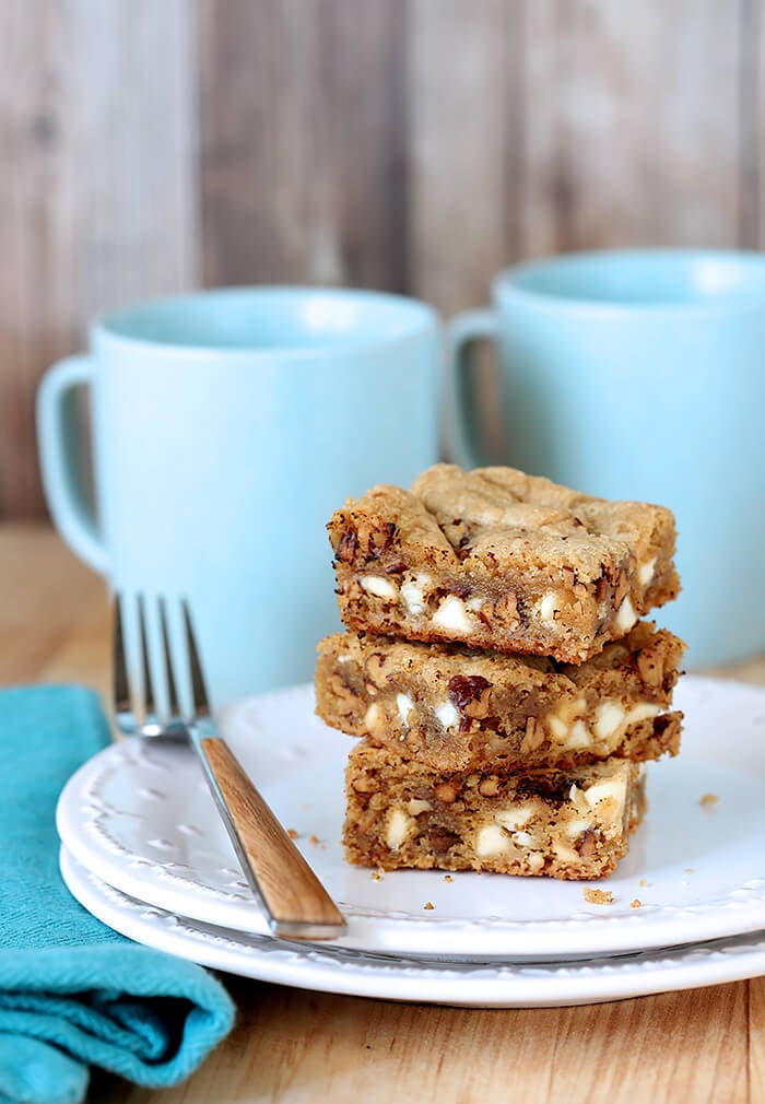 Blondies with White Chocolate Chips and Toasted Pecans on a White Plate with Aqua Coffee Mugs in Background