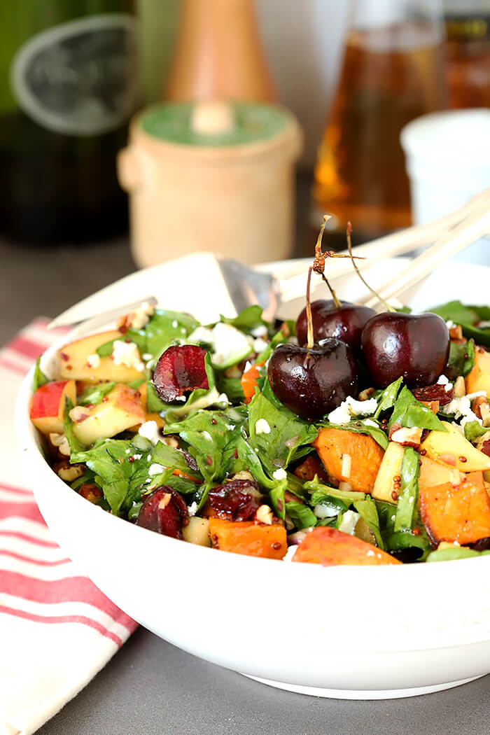 Sweet Potato and Spinach Salad with Pecans, Cherries and Goat Cheese Served in a White Bowl and Whole Cherries for Garnish