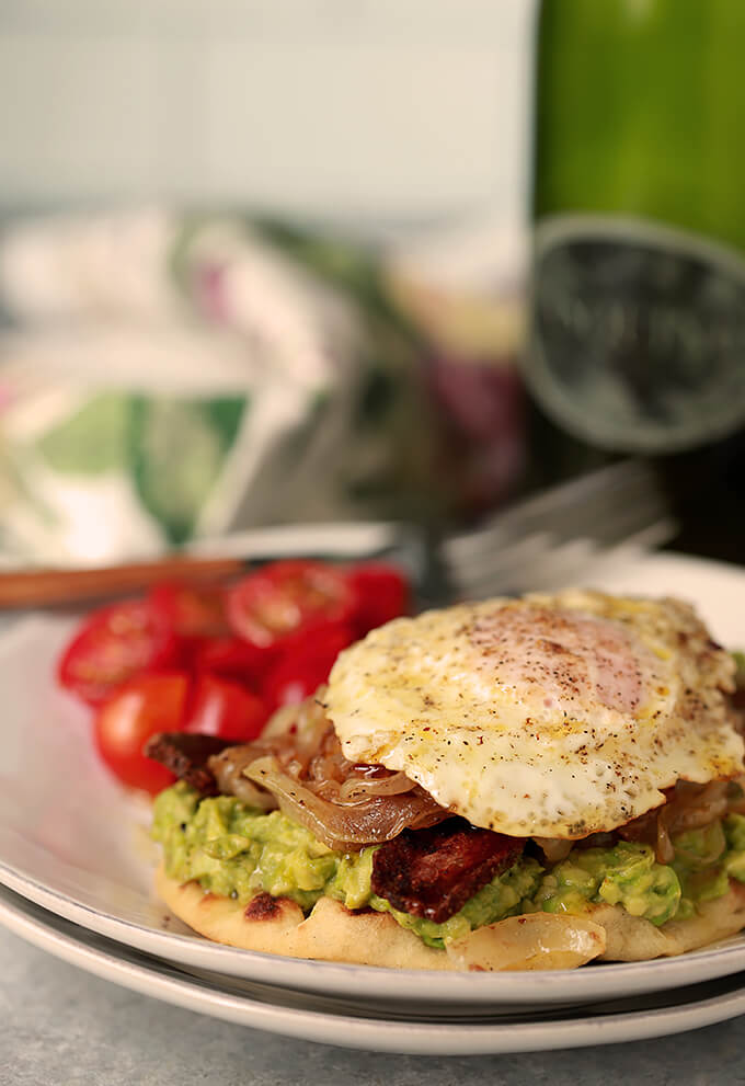 Avocado Toast with Bacon and Egg on Naan Served with Cherry Tomatoes on a White Plate