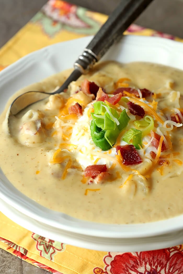 Baked Potato Soup with Leeks in a White Bowl and Garnished with Sour Cream, Cheese, Bacon Bits and Sauteed Leeks