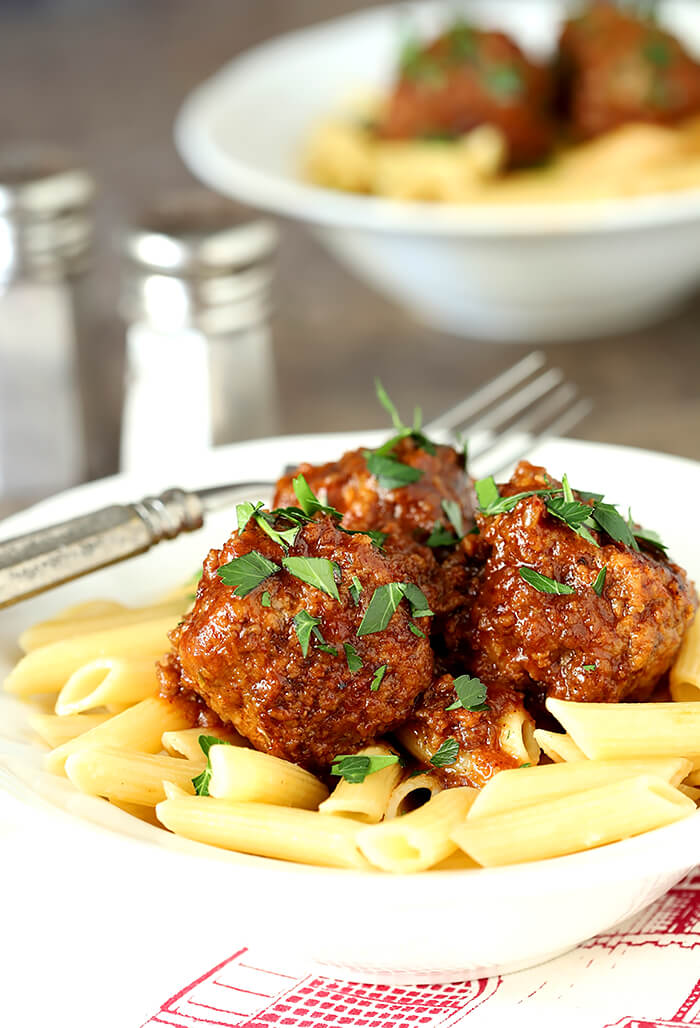 Beef, Bourbon, and Bacon Meatballs Served in a White Bowl with Penne Pasta and Parsley Garnish