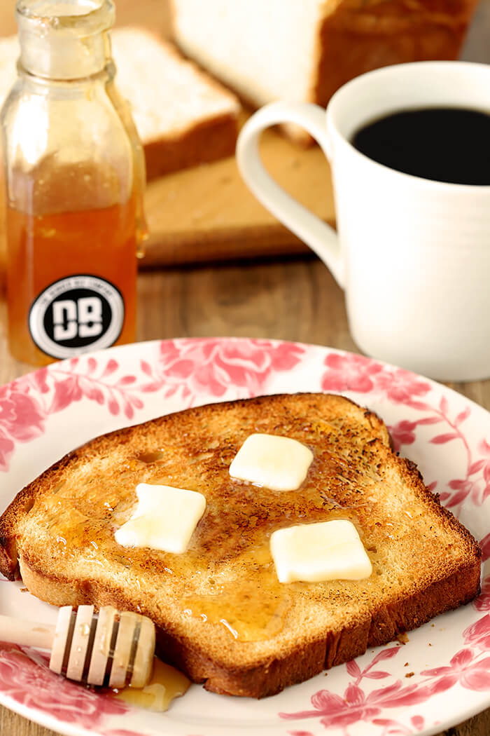 Slice of Billowy Off-White Bread with Milk and Honey Topped with Sesame Seeds and Served with Pats of Butter and Drizzled Honey