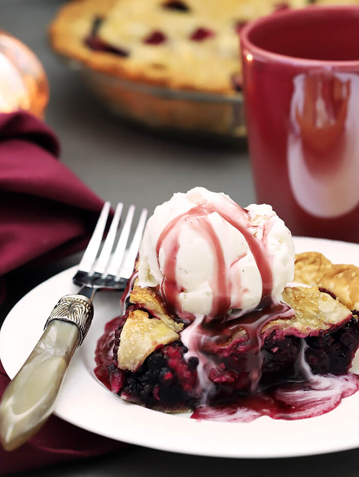 A Slice of Booberry (Mixed Berry Pie) with Vanilla Ice Cream on Top Drizzled with Pomegranate Syrup