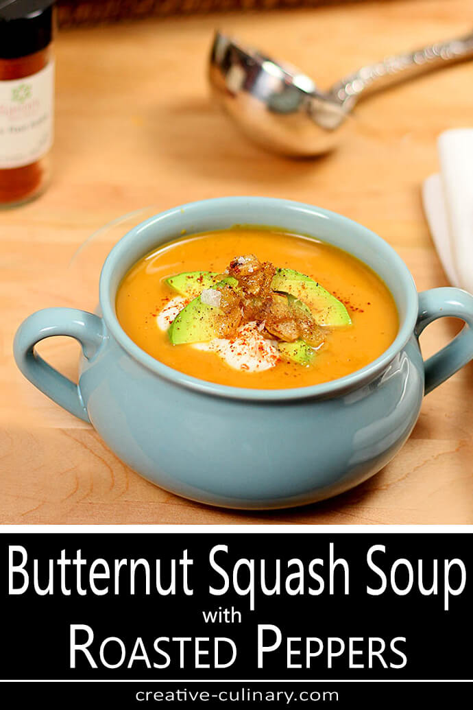 Butternut Squash Soup with Roasted Peppers in a Soup Crock and Garnished with Sour Cream and Avocado