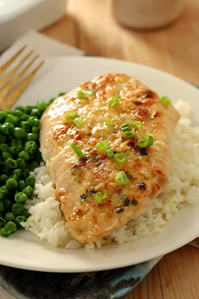Broiled Chicken Parmesan Closeup Served on a Bed of Rice with a Side of Green Peas