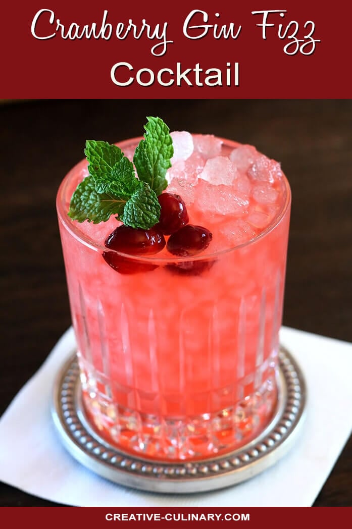 Cranberry Gin Fizz Cocktail in a cut crystal glass garnished with Cranberries and Mint.