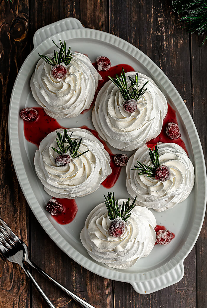Mini Pavlovas with Cranberry Curd and Whipped Cream, garnished with Sugared Cranberries and a Sprig of Rosemary