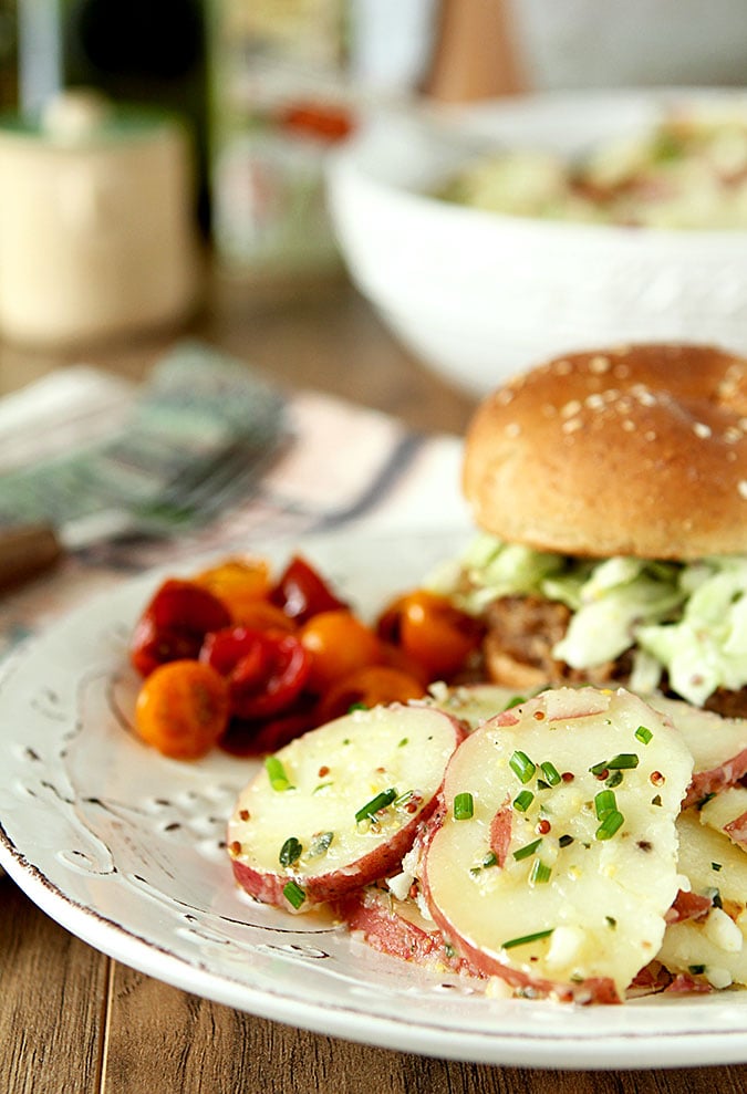 French Potato Salad with Fines Herbes French Potato Salad with Herbs on a White Plate with a Sandwich and Chopped Tomatoes