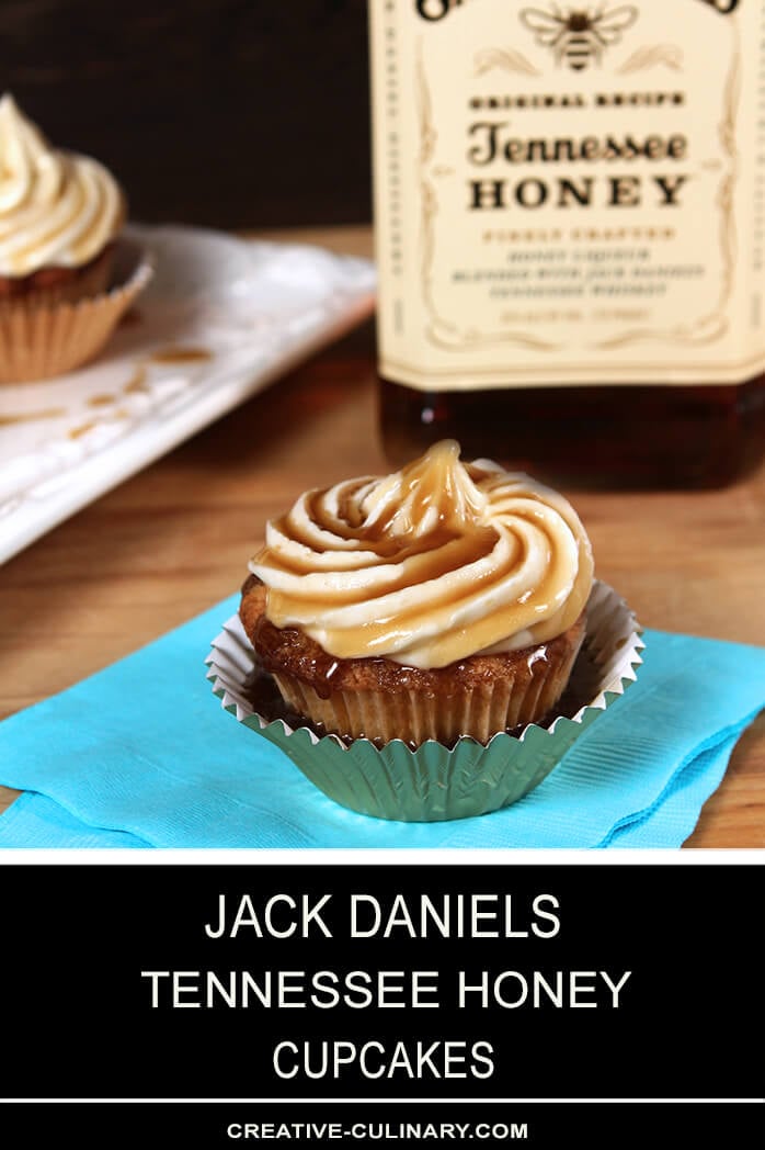 Closeup of Jack Daniels Honey Whiskey Cupcakes with a Boozy Drizzle from a Spoon In a Metallic Cupcake Liner in Front of a Bottle of Jack Daniels Tennessee Honey