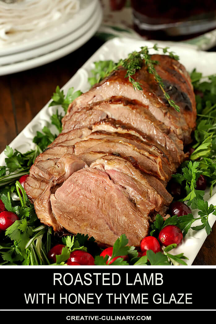 Roasted Lamb with Honey Thyme Glaze Carved and on a White Rectangular Serving Platter Garnished with Parsley and Cranberries