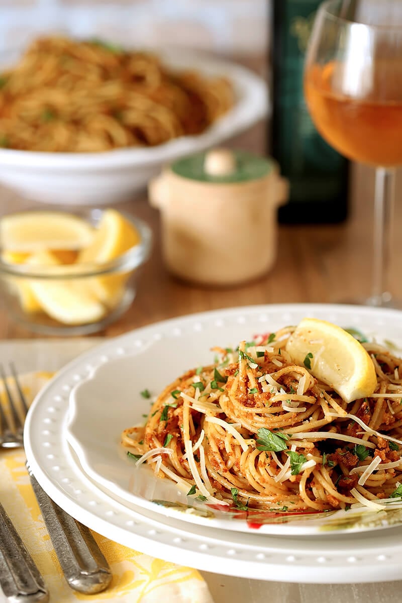 Pasta with Sun-Dried Tomato and Roasted Almond Pesto Served on a White Plate with Lemon Garnish