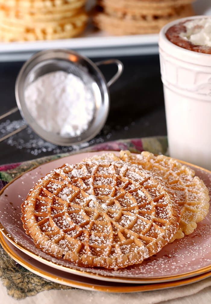 Pizzelles - Italian Waffle Cookies Sprinkled with Powdered Sugar and Served on Pink Plate