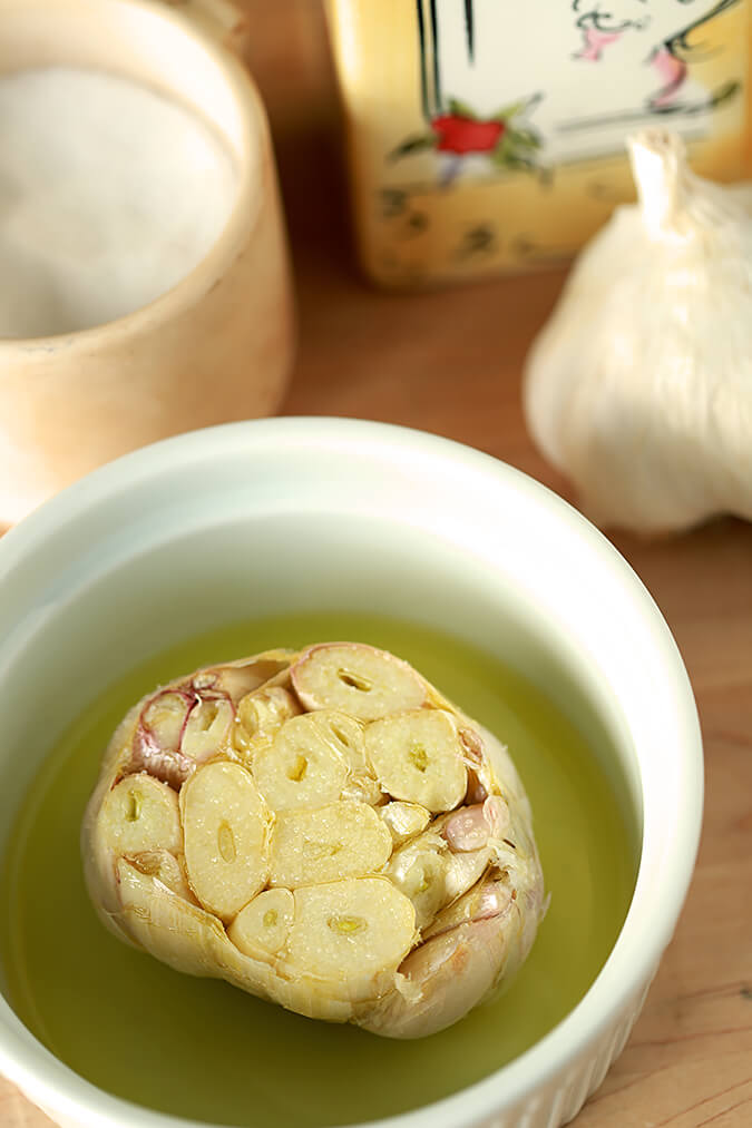 Raw garlic is in a baking dish with olive oil and salt on top.