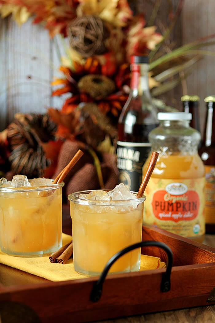Pumpkin Spiced Apple Cider Cocktail in a Lowball Glass on a Wood and Wrought Iron Tray with Bottles of Rum and Cider in the Background