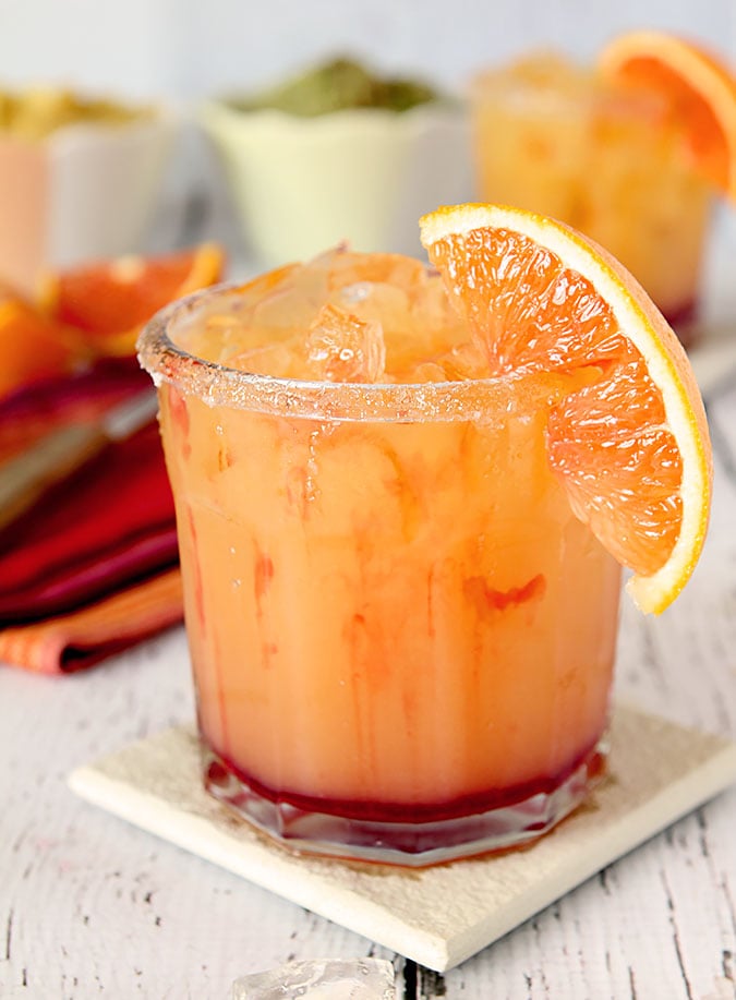 Tequila Sunrise Margarita Served in a short cocktail glass with orange juice and streaks of red grenadine.