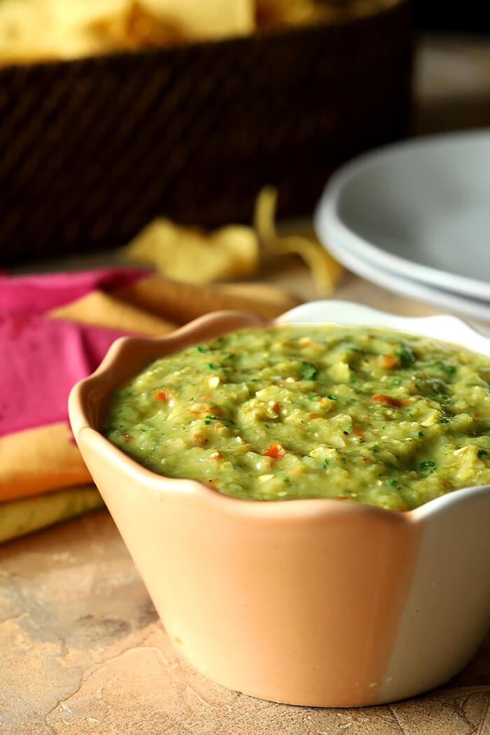 Tomatillo Salsa Verde (Green Salsa) in a Peach and White Bowl on Table with Tortilla Chips