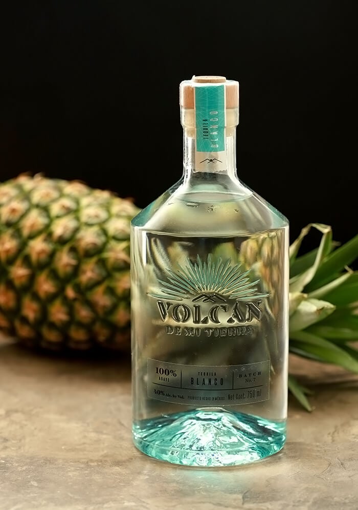 Bottle of Volcan Tequila Staged in front of horizontal pineapple